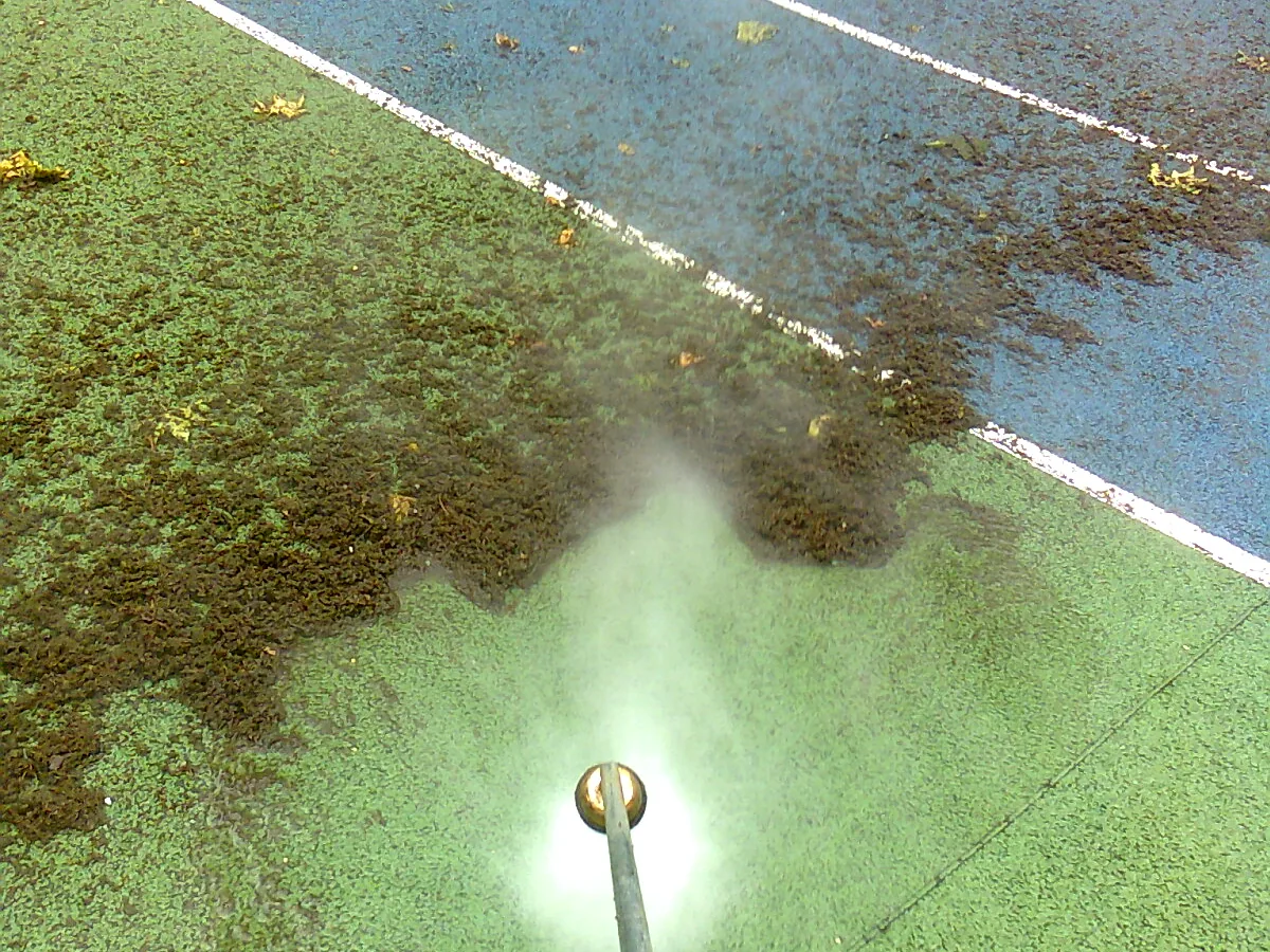 Court de tennis en cours de démoussage : moitié couverte de mousse, moitié nettoyée